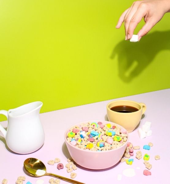 Bol de céréales colorées avec café, lait et main tenant un morceau de sucre.