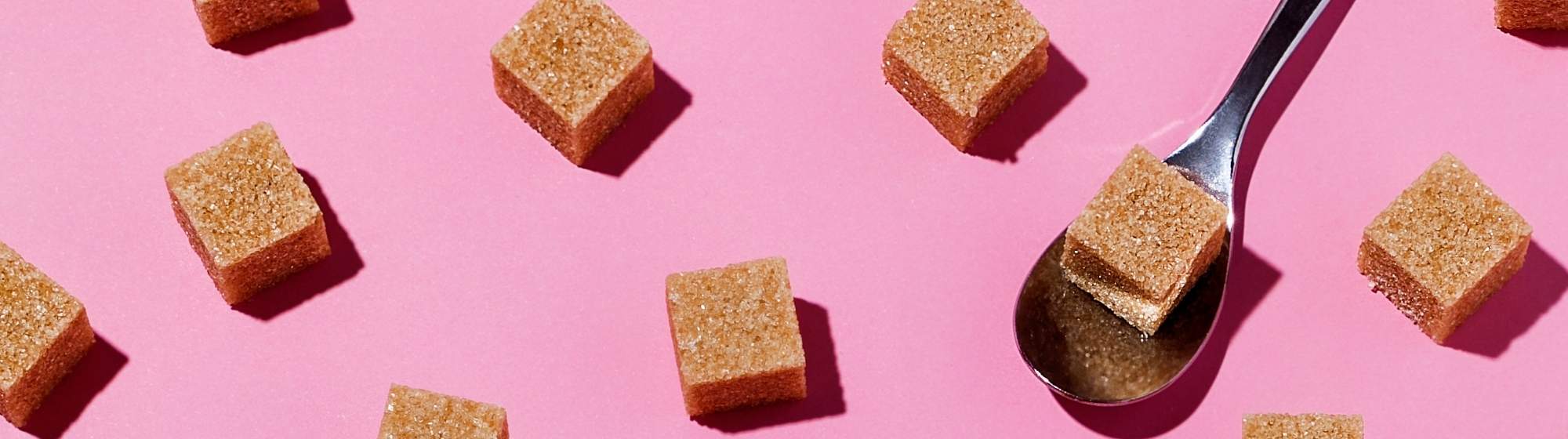 Bannière avec morceaux de sucre roux et cuillère sur fond rose.