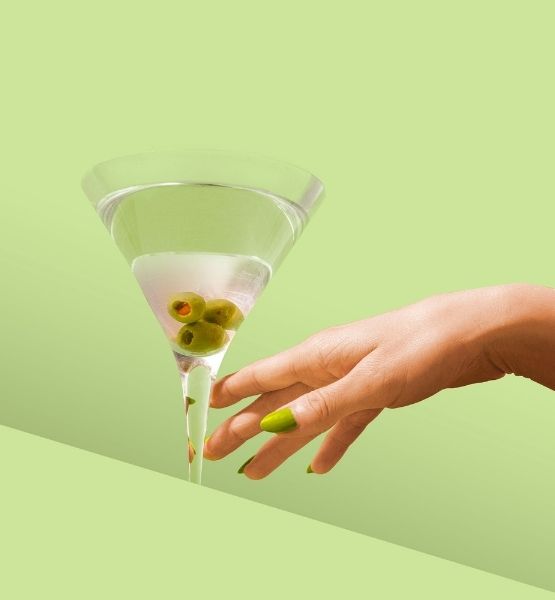 Martini glass with olives held by a hand on green background