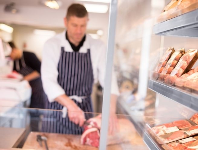 A caterer is cutting red meat in a butcher shop.