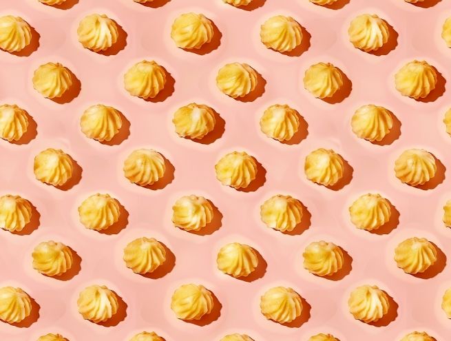 Pommes dauphine disposées en motif répétitif sur fond rose clair.