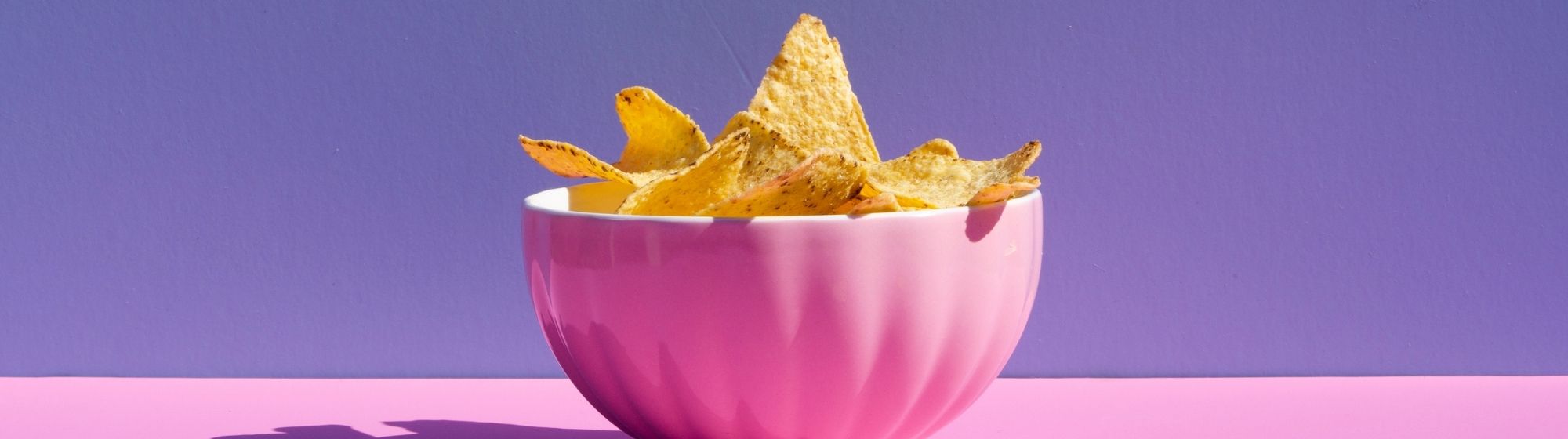 Pink bowl filled with tortilla chips on purple and pink background.