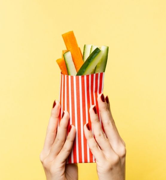 Hand holding red and white striped bag with carrot and cucumber sticks.