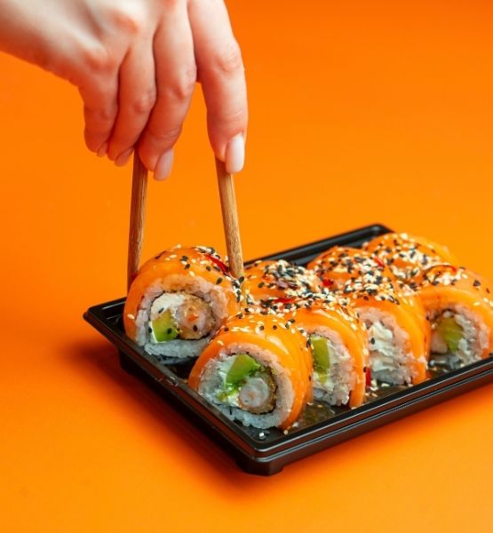 Plateau de sushis saumon avec graines de sesame sur fond orange.