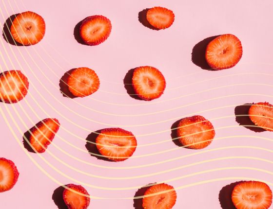 Vue aérienne de nombreuses tranches de fraises sur un fond rose clair décoré de lignes ondulées jaunes.