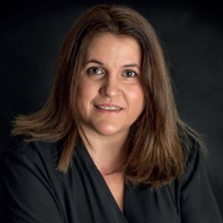 Portrait of a brown-haired woman wearing a black top, photographed against a dark background.