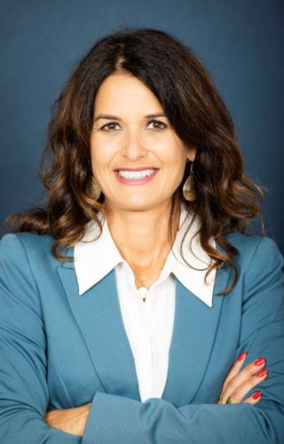 Professional portrait of a smiling person in a blue blazer and white shirt, arms crossed against a blue background.