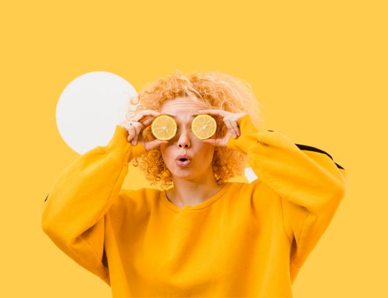 Personne en sweat jaune tenant deux rondelles de citron devant ses yeux sur un fond jaune vif.